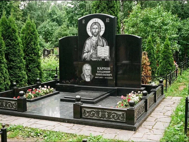 Памятник с гравировкой иконы: широкая панорамная стела с золочёным нимбом — гравировка образа Матроны Московской, цветник с белыми хризантемами, работа «Мельникова» в Казани