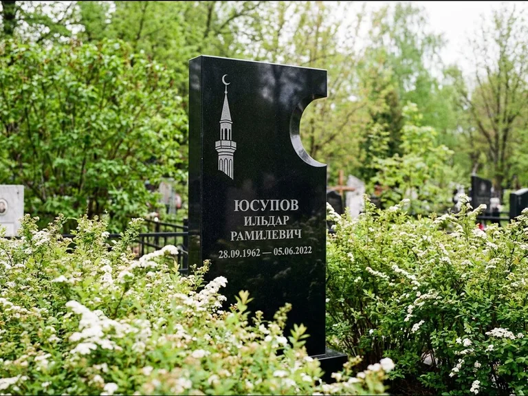 Мусульманский памятник с гравировкой мечети: стела с боковым вырезом в форме полумесяца — гравировка минарета с полумесяцем, низкие кусты спиреи в цвету, работа «Юсупов» в Казани